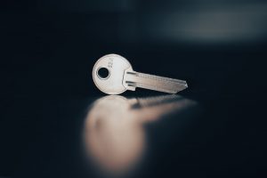 A silver key and a blurry reflection of the key on a dark table with a blurred background.