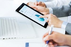 Close up of hands on table, one holding tablet with data visualizations on it